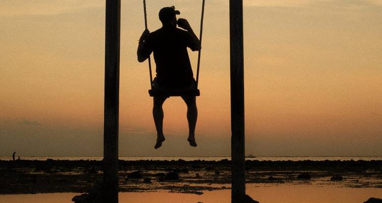 Silhouette d'une personne sur une balançoire au coucher du soleil.