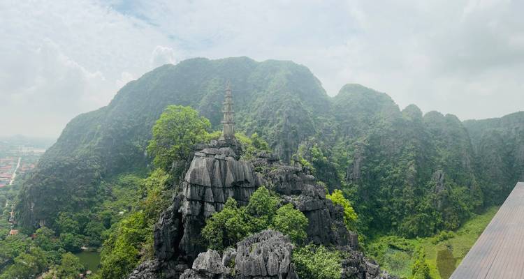 Vue d'une formation rocheuse avec une petite pagode au sommet sur un arrière-plan de montagnes vertes.