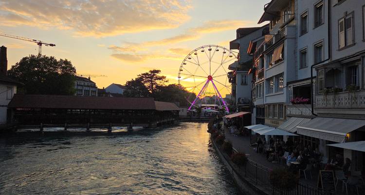 Une vue du coucher de soleil sur une rivière avec une grande roue et des bâtiments