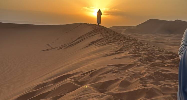 Silhouette of a person standing on sand dune at sunset.
