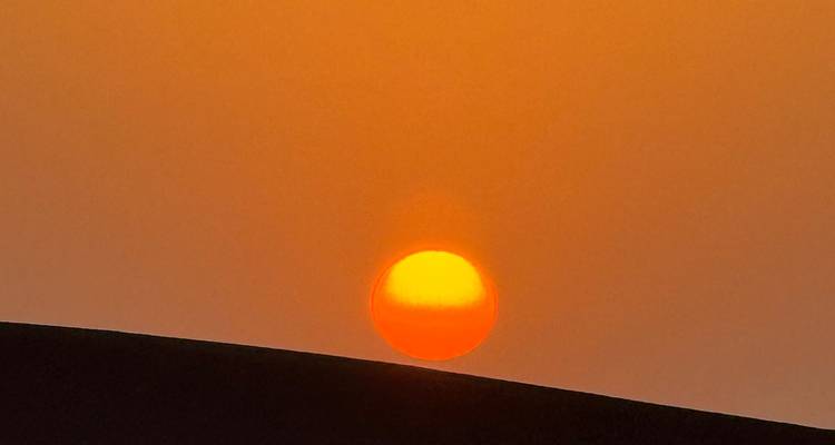 Soleil orange vif se couchant sur une dune de sable.