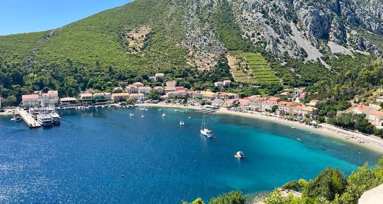 Vue panoramique d'un village côtier avec de l'eau bleue et des collines vertes.