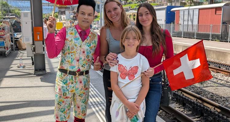 Un groupe de personnes posant dans une gare en tenant un drapeau suisse.