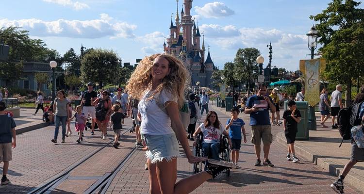 Une femme posant joyeusement devant un parc d'attractions sur le thème des châteaux.