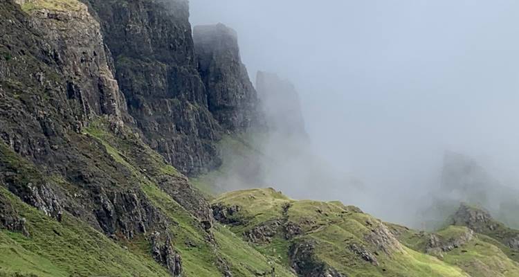 Vue brumeuse de falaises escarpées et de collines verdoyantes.