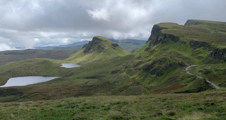 Une vue panoramique de collines verdoyantes ondulantes et de petits lacs sous un ciel nuageux.