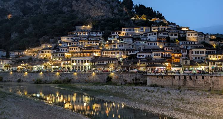 Vue nocturne de Berat, mettant en valeur les maisons historiques illuminées le long de la rivière.