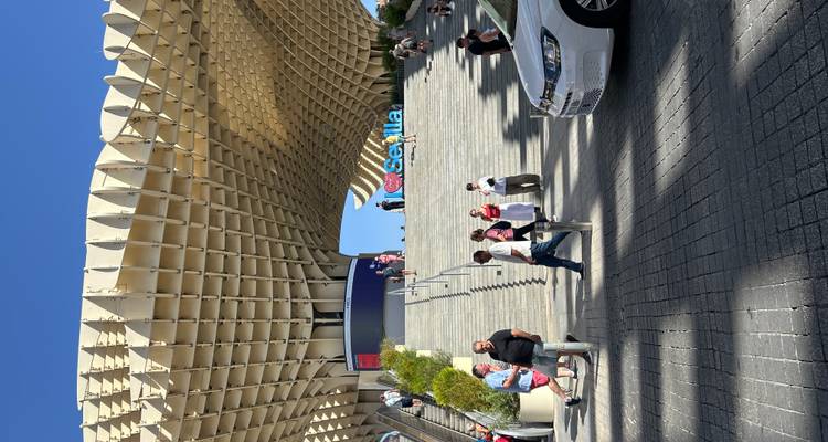 Personnes marchant sous une structure architecturale moderne avec un panneau 'Sevilla'.