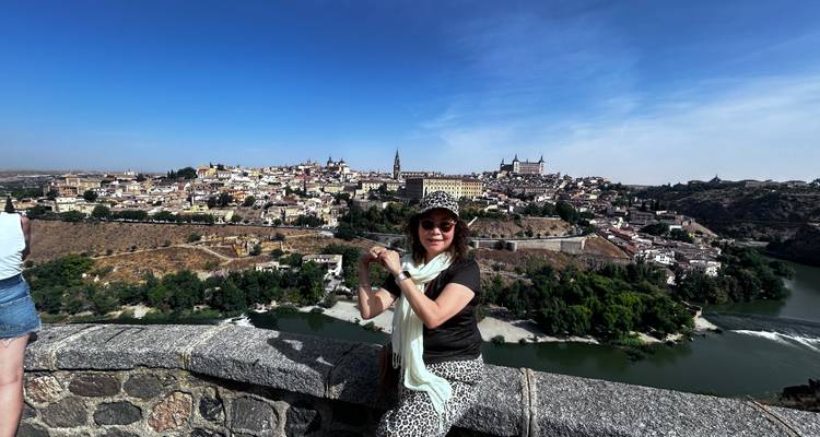 Femme posant près d'un mur de pierre avec vue sur une ville de l'autre côté d'une rivière.