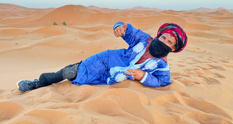 Personne en tenue traditionnelle posant sur le sable du désert.