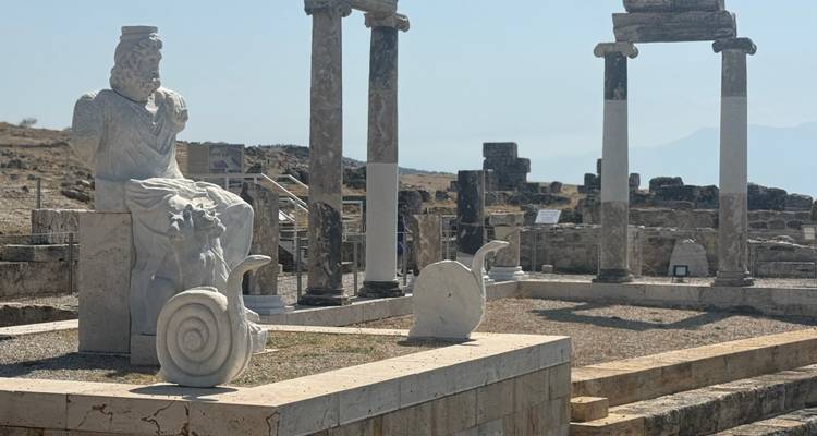 Ancient Greco-Roman ruins with columns, statues, and a seated deity statue.