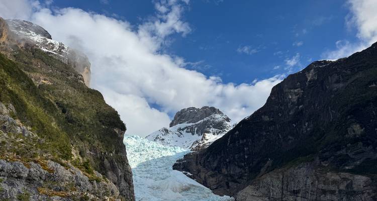 Dichtbijzicht van een gletsjer genesteld tussen bergkliffen onder een blauwe hemel.