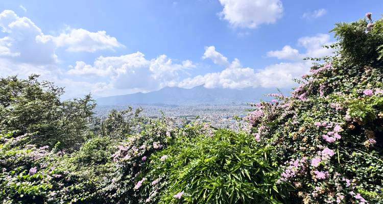 Wide view of a cityscape beneath a bright blue sky with fluffy clouds, possibly Kathmandu.