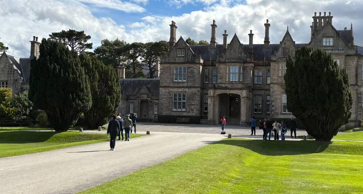 Des personnes marchant vers un bâtiment historique avec de l'herbe soigneusement taillée devant.