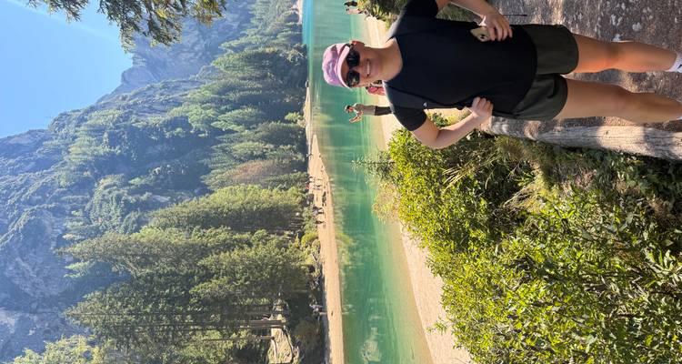 Personne au bord d'un lac turquoise avec des montagnes boisées.