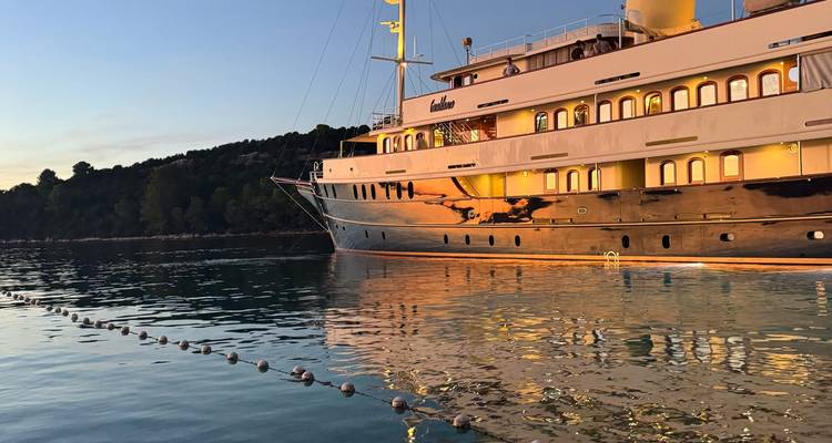 Grand yacht amarré sur une eau calme au coucher du soleil avec un reflet dans l'eau.