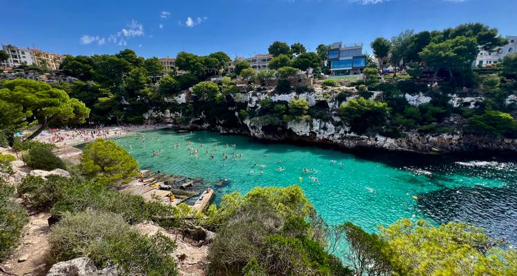 Anse avec une eau claire et des gens qui nagent, entourée de verdure.