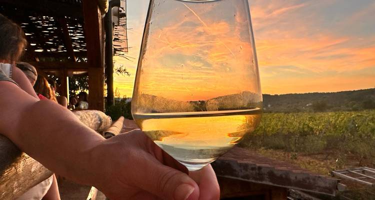 Main tenant un verre de vin avec un coucher de soleil en arrière-plan.