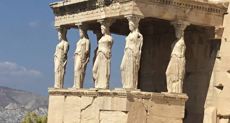 The Caryatids of the Erechtheion on the Acropolis, with city and mountain in the background.