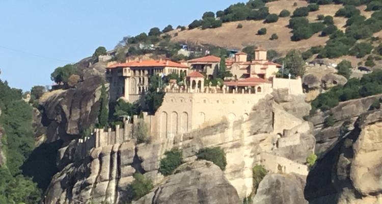 A monastery perched on a rock formation surrounded by greenery.