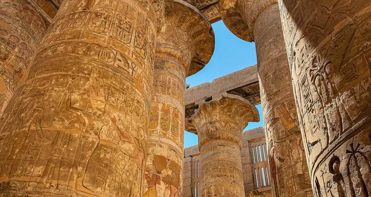 Colossal stone columns with intricate hieroglyphs under blue sky.