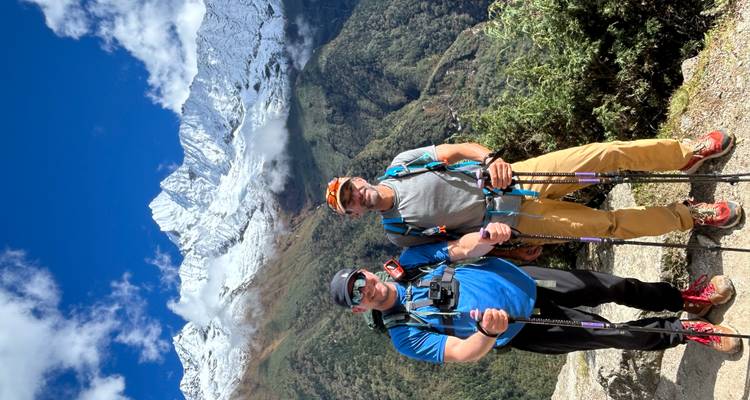 Two people posing with hiking poles in front of snow-capped mountains.