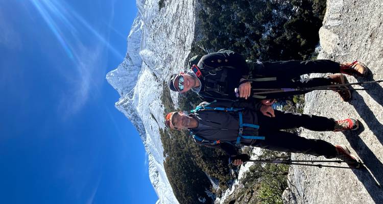 Two hikers standing with snow-covered mountain peak in the background.