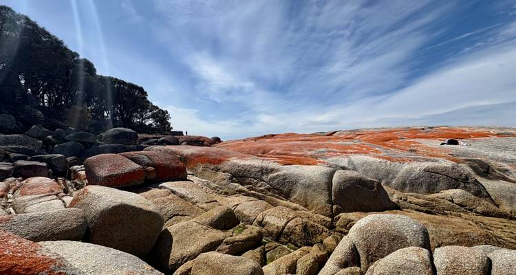 Rocky coastline with red and orange rocks under a blue sky.