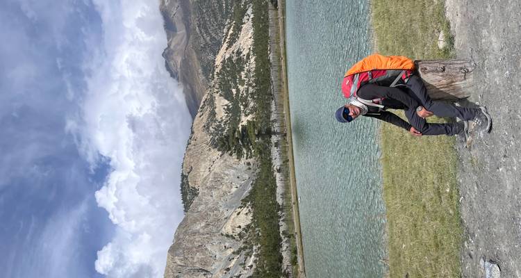 Personne se reposant sur un tronc d'arbre au bord d'un lac serein avec des montagnes en arrière-plan.