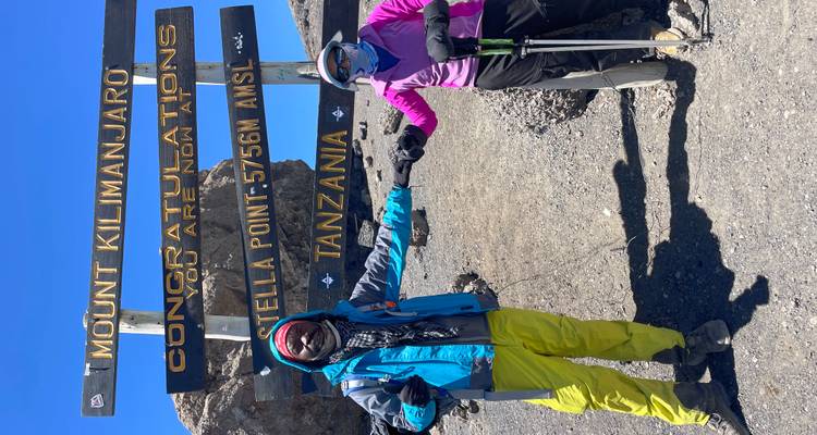 Two people posing in front of a sign at Stella Point on Mount Kilimanjaro.