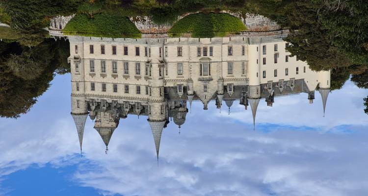 Grand château historique situé sur une colline verdoyante avec un ciel nuageux.