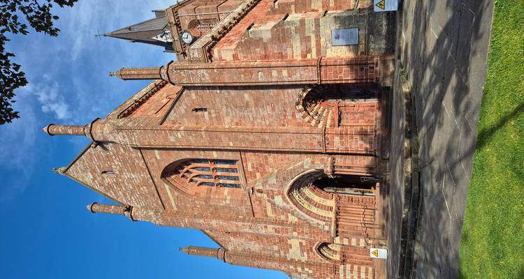 Une cathédrale historique avec une architecture en pierre rouge sous un ciel bleu dégagé.