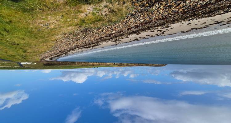 Une vue panoramique d'une plage avec une eau bleue claire et un ciel nuageux.