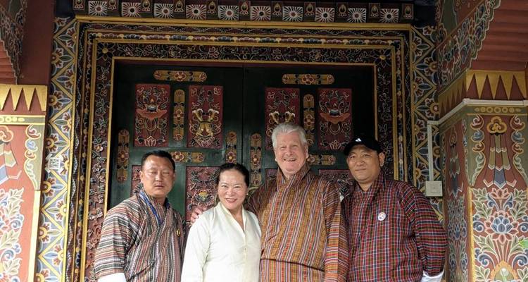 Four people in traditional Bhutanese attire posing at an ornately decorated entrance.