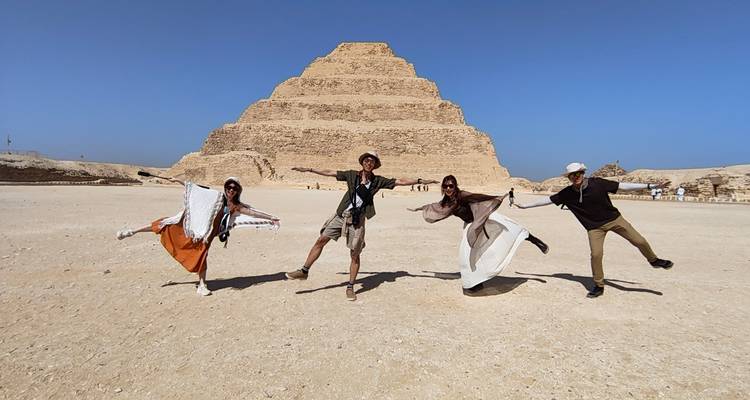 Four people posing in front of a pyramid on a sunny day.