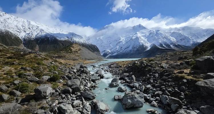 Mountain stream with rocks and snow-capped peaks.