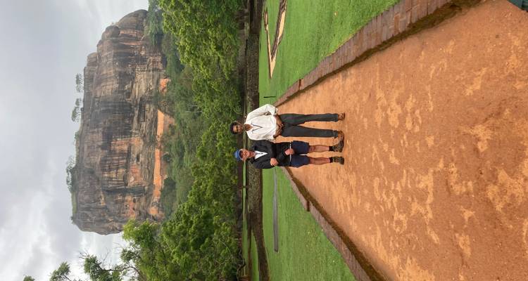 Two people posing on a path with a large rock formation in the background.