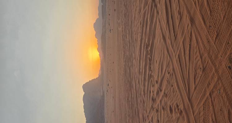 Sunset over a wide expanse of desert with tracks in the sand.