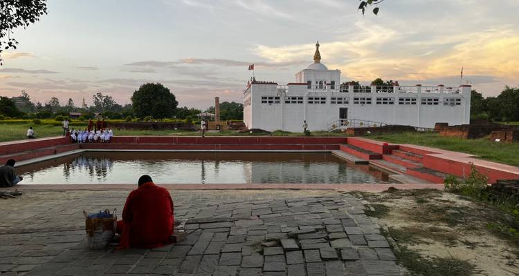 An individual seated facing a rectangular pond with a white temple in the background.