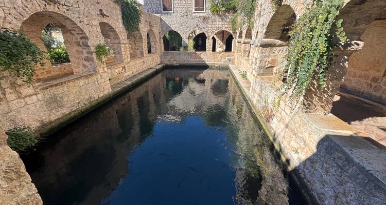Cour en pierre avec un bassin d'eau claire et des arches en pierre.