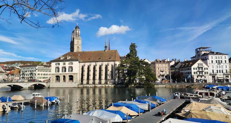 Une rivière avec des bateaux et des bâtiments historiques en arrière-plan, avec un ciel bleu clair.