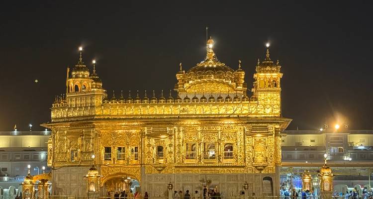 Golden temple lit up at night reflecting over water.