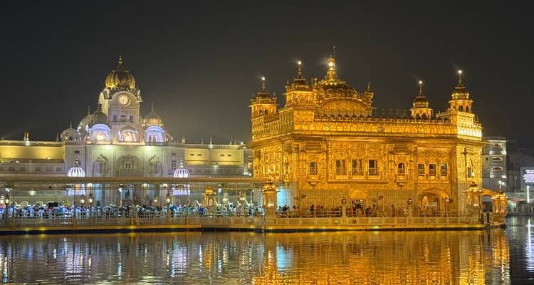 Lit up Golden Temple with people on the banks nearby.