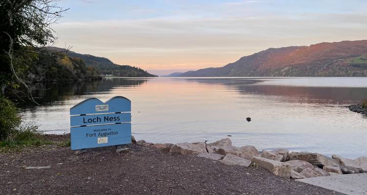Loch Ness avec un panneau et un lac calme sous un ciel de coucher de soleil.