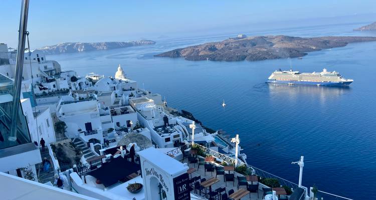 Vue imprenable sur une île méditerranéenne avec des bâtiments blancs et un navire de croisière en mer.
