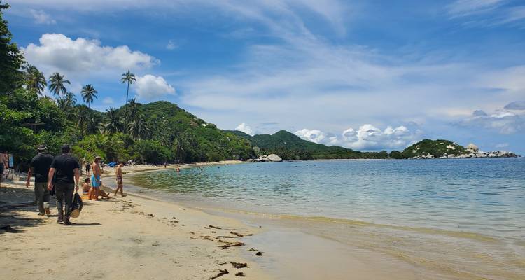 Plage de sable avec des gens au bord de l'eau, végétation luxuriante alentour.