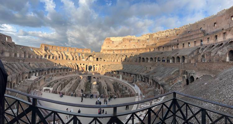 Interior view of the Colosseum under clouds with visitors around.
