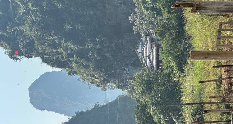Pavillon chinois traditionnel entouré de verdure luxuriante et de montagnes.