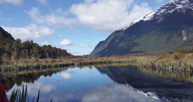 Lago tranquilo con reflejos de montañas y cielo azul.