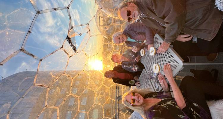 Groupe de personnes savourant des boissons à l'intérieur d'un dôme avec vue sur le coucher de soleil.